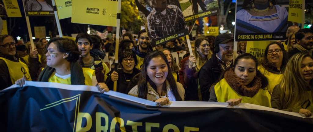 a group of amnesty activists, holding signs and placards and wearing white and black shirts, protest for our right to a safe and healthy planet. 